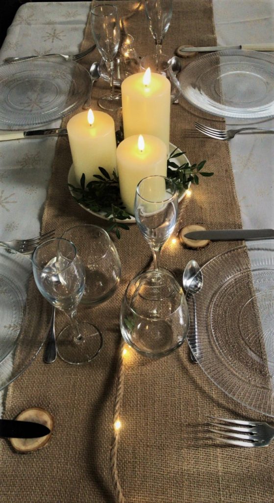 table de Noël réussie avec bougies chemin de table en toile de jute guirlande micro led et rondins en bois